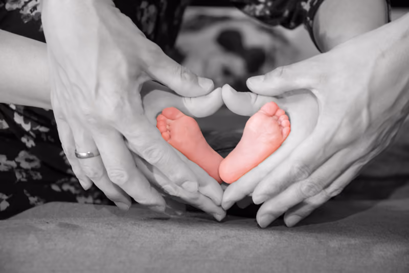 Elternhände formen ein Herz um zwei Babyfüße