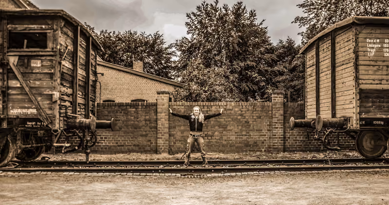 Person mit ausgebreiteten Armen zwischen zwei alten Güterwaggons, in Sepia