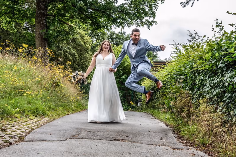 Brautpaar springt Hand in Hand über eine Wiese