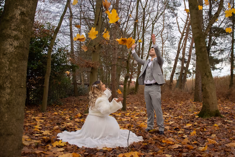 Brautpaar wirft im Herbstwald bunte Blätter in die Luft
