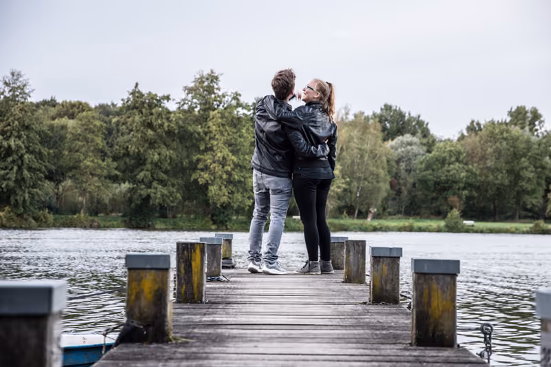 Paar steht Arm in Arm auf einem Holzsteg am See