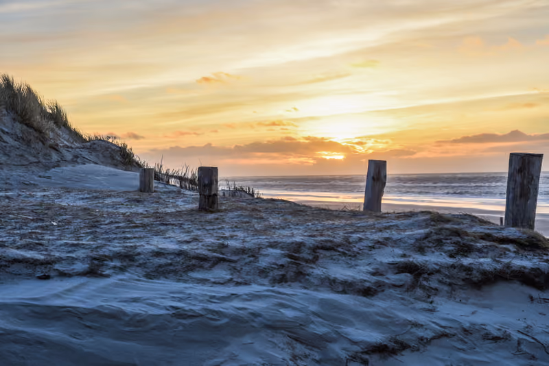 Sonnenuntergang am Strand von Texel mit Holzpfählen im Sand